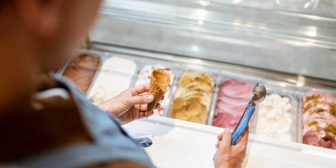 Salesman picking ice cream with a spoon from refrigerator in the shop Salesman picking ice cream with a spoon from refrigerator in the shop